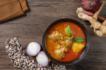 Chicken massaman curry in black bowl with herb and spices on wooden background. Thai authentic food called massaman kai. top view. Flat lay.