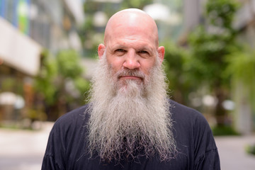 Face of mature handsome bald bearded man with nature in the city