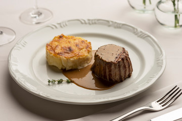 Fillet mignon tenderloin with potatoes gratin and green poivre vert sauce gravy on white with wine and water glass.