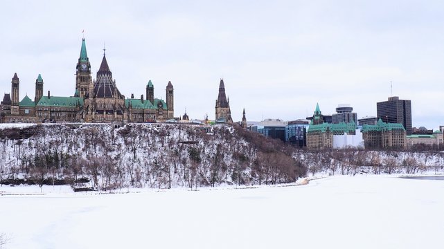The Parliament Building on Canada stands tall on Parliament Hill on a cold winter day, with the Ottawa River still frozen from the dog days of winter.
