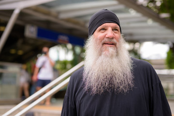 Happy mature handsome bearded hipster man thinking outside the subway train station