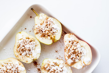 Halves of pears with nuts, cinnamon and icing sugar on a white background. Dessert recipe
