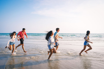 Fototapeta na wymiar Group of friends running having fun on the white sand beach amid the blue sky. Concept of Summer, sea and beach.