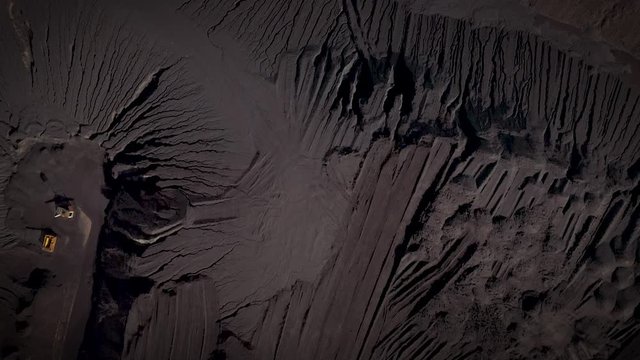 An aerial shot of a large open-pit coal heap. Coal mine with equipment in.