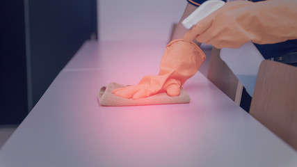 Woman hand in protective orange rubber gloves holding green microfiber cleaning cloth and wiping dust using a spray sterilizing solution make cleaning and disinfection for good hygiene