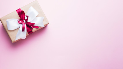 Gift or present box with a big bow on a pink table top view. Flatlay composition for Christmas birthday, mother day or wedding.