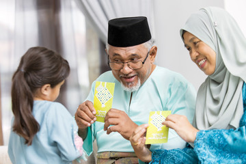 Senior Muslim couple showing green envelopes to their granddaughter