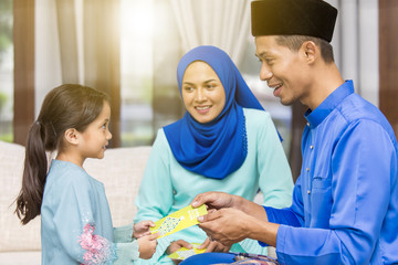Muslim girl receiving green envelopes from parents during Eid al-Fitr