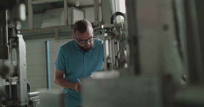 The engineer in glasses with notebook examining a serviceability of machine