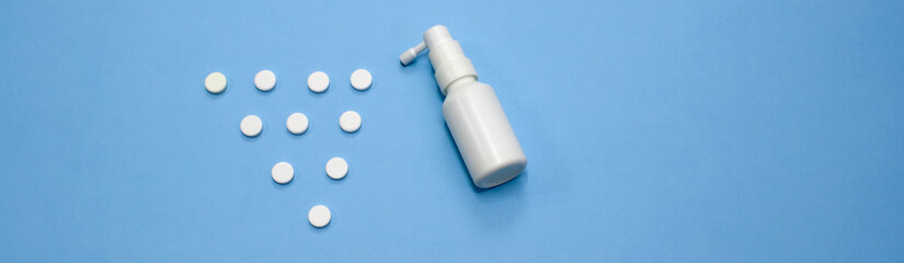 White plastic bottle spray and white pills are scattered in triangle shape on a blue background. Treatment of patients for the virus. Strengthening the immune system. Web banner.