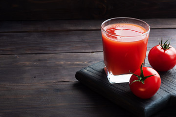 Tomato juice in glass glasses and fresh ripe tomatoes on a branch. Dark wooden background with copy...