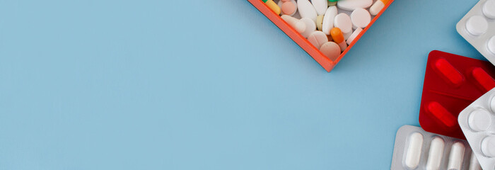 Packs of colorful pills, drugs and capsules and box with assorted pills on a blue background. Prevention of coronavirus. Web banner with empty space for text. Isolated. Medical preparations close up