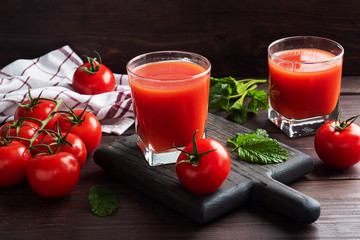 Tomato juice in glass glasses and fresh ripe tomatoes on a branch. Dark wooden background with copy space.
