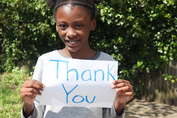 Kid smiling while holding Thank You placard sign outside with green bushes in background