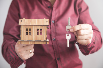 Man holding house keys with house model in office.