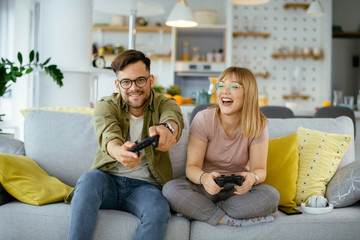 Husband and wife playing video game with joysticks in living room.
Loving couple are playing video games at home.