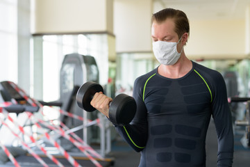 Young man with mask exercising with dumbbell at gym during corona virus covid-19