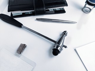 A stethoscope, a neurologist's hammer, a doctor's seal, a pen, and a black Notepad on a white background.