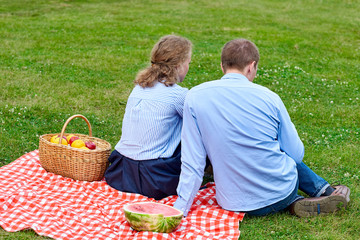 Young couple in love on picnic sitting on tablecloth in red cell. Love couple resting in nature in...