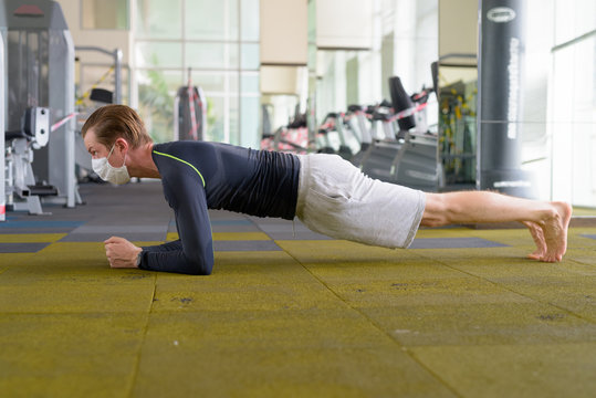 Full Body Shot Of Young Man With Mask Doing Plank Position On The Floor At Gym During Corona Virus Covid-19