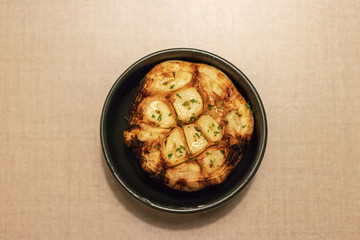 Garlic clove grilled in black bowl in warm light at steakhouse. 