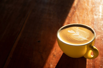 Cup of coffee with latte art on wooden table and morning sunlight; copy space. 
