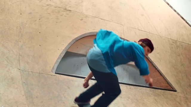 Lockdown of male Caucasian skater wearing jeans, hat, blue shirt and sneakers performing difficult trick on skateboard