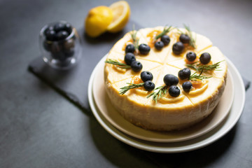 Homemade cheesecake with fresh blueberry and candied lemon on black stone background.