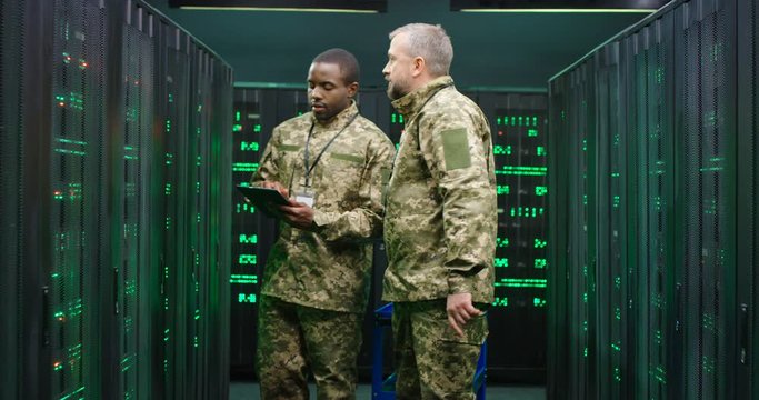 Mixed-races Army Technicians In Camouflage Uniforms Checking Servers In Data Analytic Center. Caucasia And African Male Colleagues Of Cybersecurity Military Facilities.