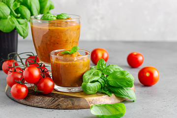 Summer homemade cold tomato cream soup in glass. Traditional Spanish soup gazpacho with basil. Grey concrete background.