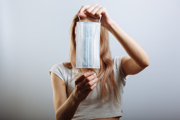 Young beautiful woman put on medical mask for protection against coronavirus contagious disease. on a light background. Medic holding face mask. Preventive measure against coronavirus COVID-19