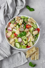 Vegetarian fattoush salad. Traditional Middle Eastern salad with toasted pita bread and vegetables. Lebanese cuisine. Light grey stone background. Top view.