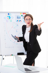 Emotional woman trainer in the office in a business suit shows charts on a flipchart, explains the strategy and motivates for success