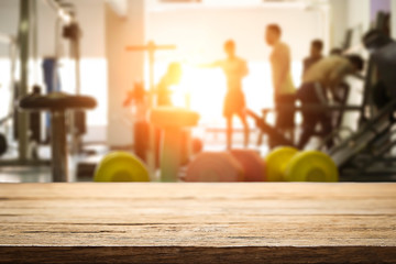 Empty wooden desk space over  blur fitness gym background. For product display montage. Business presentation.