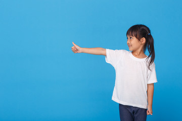 Happy child, little girl showing thumbs up gesture in a white T-shirt isolated on blue background. Space for Your Text. OK sign