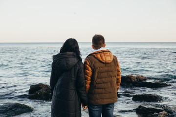 Rear view of a heterosexual couple holding hands and looking at the ocean.