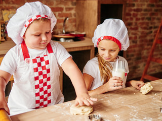 Children enjoying kneading the dough in the kitchen. Boy and Girl at the kitchen. Family housekeeping