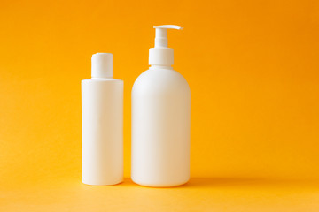 Cosmetics, moisturizer, two white plastic bottles with shower gel and shampoo on yellow background. Set of body and hair care products.