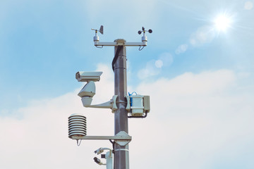 Automatic weather station, with a weather monitoring system and video cameras for observation. Against the background of blue sky the sun shines with a glare.