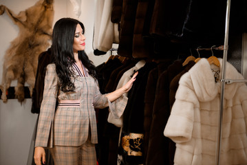 Girl customer examining new fur coat in womens cloths store