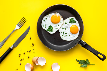 Fried eggs on frying pan on yellow desk top-down