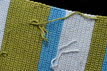 Fragment of crocheted fabric from green, blue and light blue threads close-up, top view. Abstract background. Hand made concept