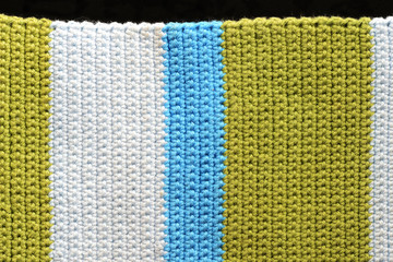 Fragment of crocheted fabric from green, blue and light blue threads close-up, top view. Abstract background. Hand made concept