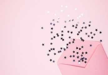 Shiny confetti stars pours from a pink envelope on a pastel pink background, top view. Flat lay. Holiday, greeting or good news concept