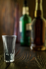An empty tequila glass in front of many colorful liquor bottles, shallow depth of field, selective focus.