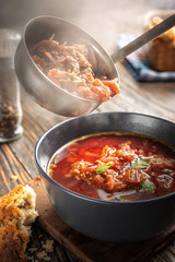 Borsch is poured into a bowl from a ladle from which steam, a traditional Ukrainian vegetable soup made from beets, carrots, tomatoes, potatoes, cabbage, herbs and garlic, close-up, shallow depth of