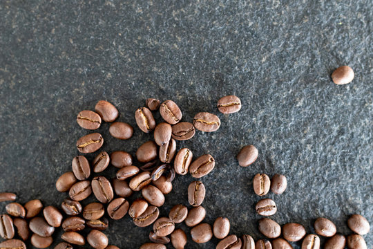 Coffee beans on black stone background. Group of coffee beans on the side of image and copy space for text.