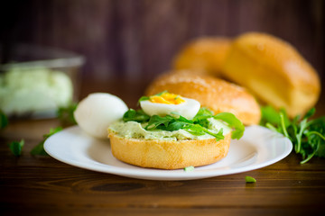 Homemade bun with cheese spread, fresh arugula and boiled egg in a plate