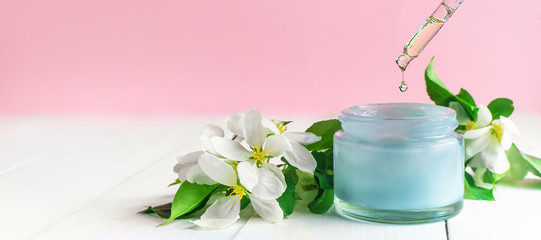 jar of cream and white flowers. Pipette oil drips into cream