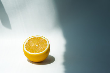 half a juicy ripe yellow lemon on a white background with hard shadows in natural light